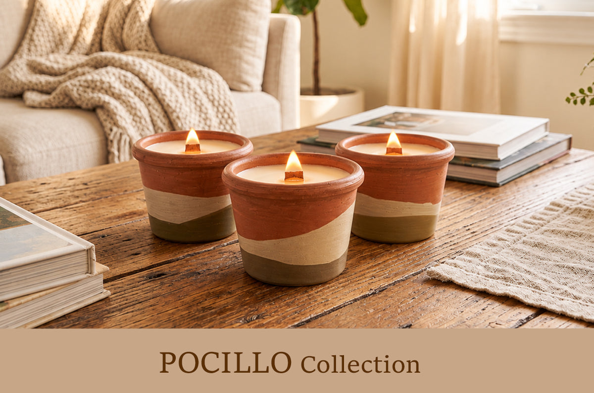 Three lit ceramic candles in terracotta, cream, and olive-green striped tumblers on a rustic wooden table in a cozy living room setting, with a sofa and books in the background. Text overlay at the bottom reads 'POCILLO Collection'.