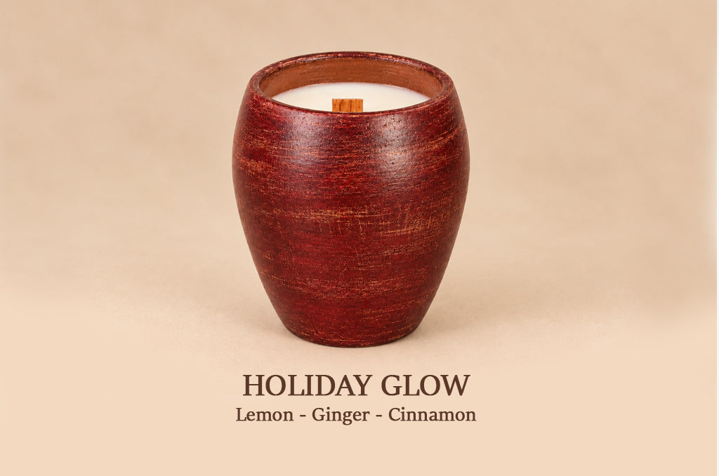 A wooden candle holder with a textured reddish-brown finish, containing white wax and a small wooden wick, set against a solid beige background with the text 'HOLIDAY GLOW Lemon - Ginger - Cinnamon' below.