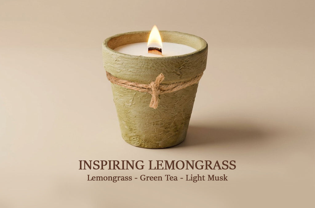 A single lit candle in a textured, terracotta-colored ceramic pot with a natural jute twine bow around the middle, set against a solid beige background. Text below reads 'INSPIRING LEMONGRASS' and 'Lemongrass - Green Tea - Light Musk'.